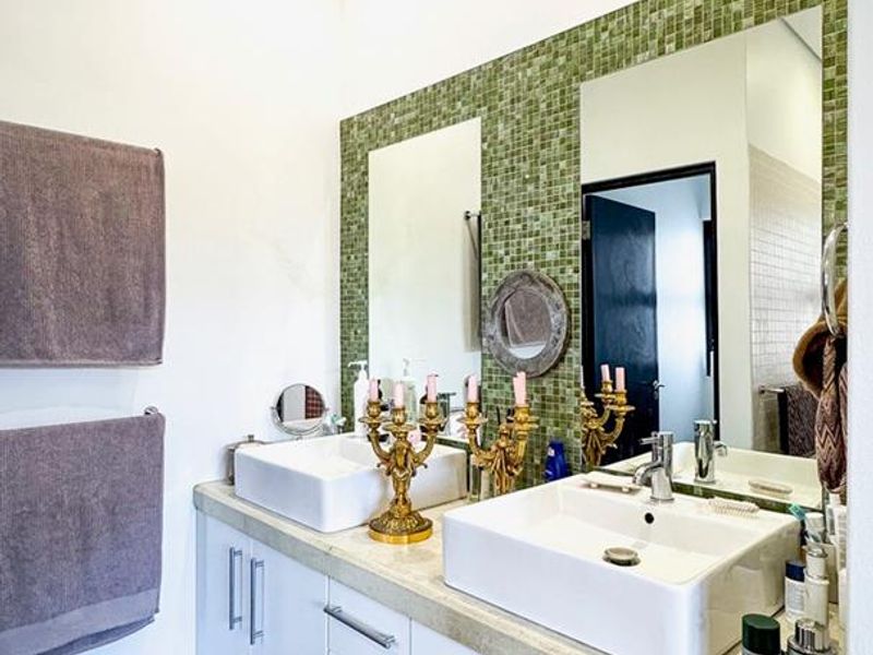 A modern bathroom featuring a double vanity with vessel sinks, a green mosaic tile backsplash, and polished concrete flooring.
