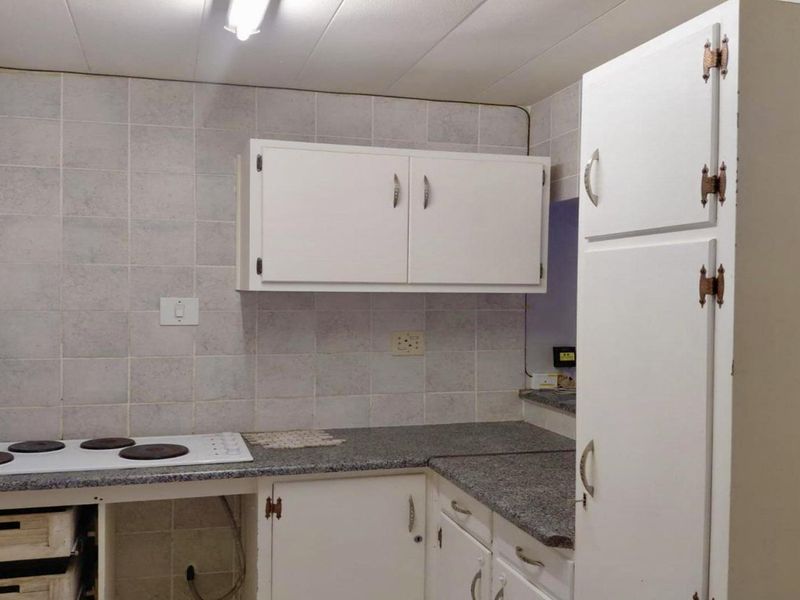 A functional kitchen featuring white cabinetry, laminate countertops, and a tiled splashback, offering potential for modernization and cosmetic updates.