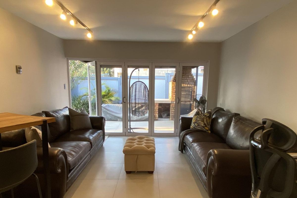 A bright living room featuring modern track lighting, large bi-fold glass doors providing seamless access to the outdoor patio area, and neutral tiled flooring.