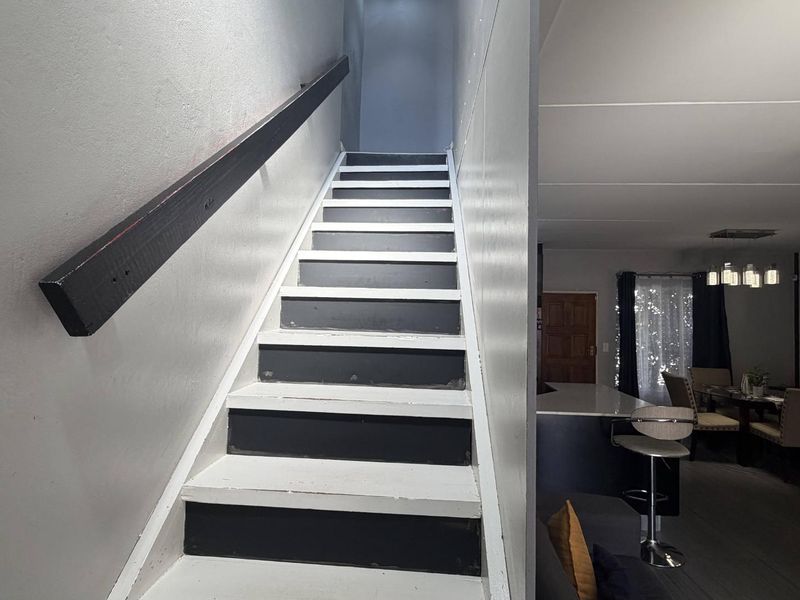 A staircase with a handrail leading to an upper level, adjacent to an open-plan living and dining area with a kitchen island.