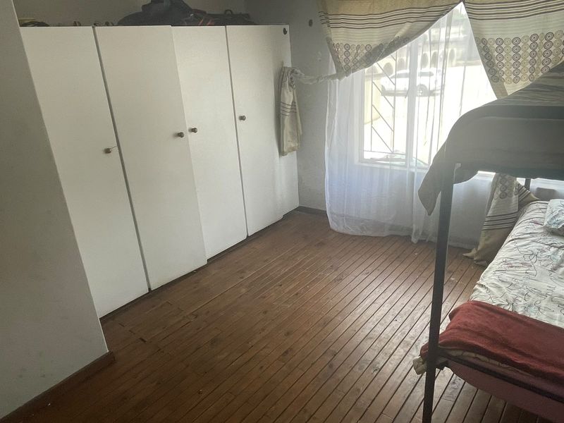 Bedroom featuring built-in cupboards, wooden flooring, and a window with security bars.