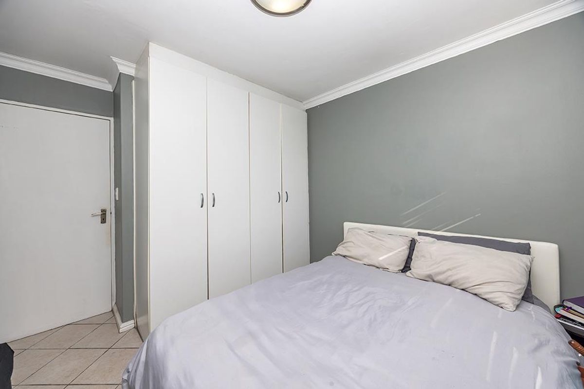 A functional bedroom featuring built-in cupboards, crown molding, and tiled flooring, providing a clean and neutral space.