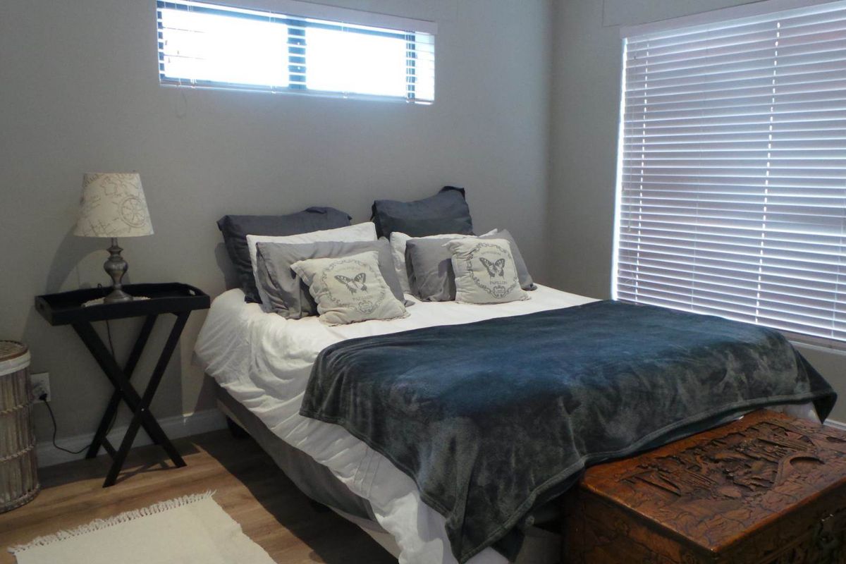 A well-maintained bedroom featuring neutral wall tones, light wood-look flooring, and horizontal window blinds providing natural light.