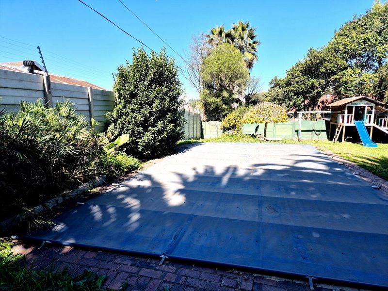 Outdoor pool area featuring a fitted pool cover, paved surround, and secure precast concrete boundary wall with electric fencing.