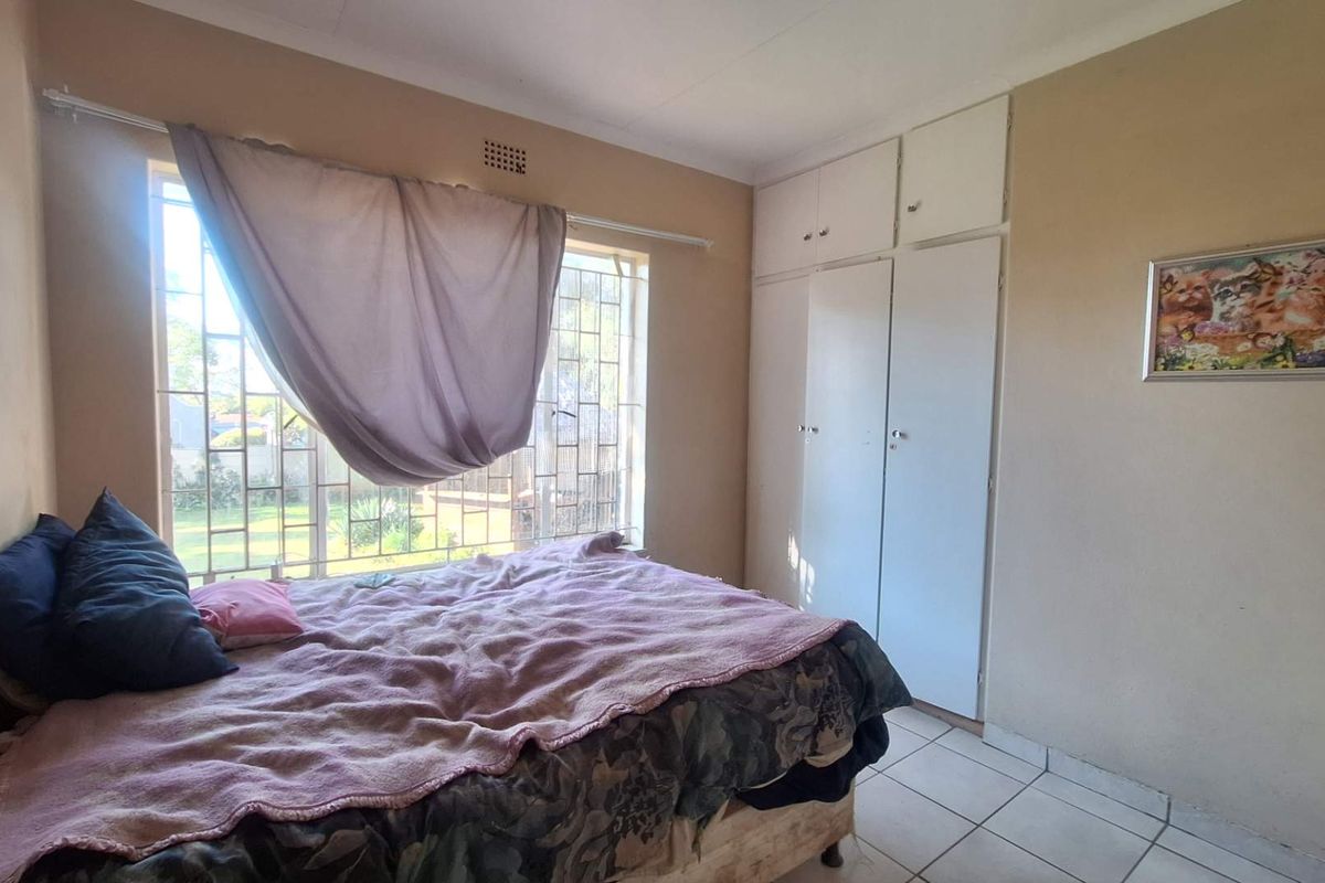 A bedroom featuring built-in cupboards, tiled flooring, and security bars on the window. The room requires cosmetic updates to improve its overall condition.