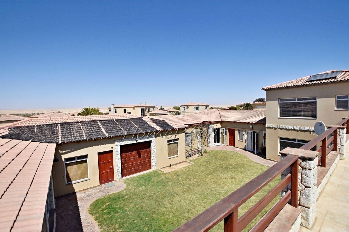 Elevated view of the rear courtyard featuring a manicured lawn, paved pathways, and access to the garage and main dwelling.