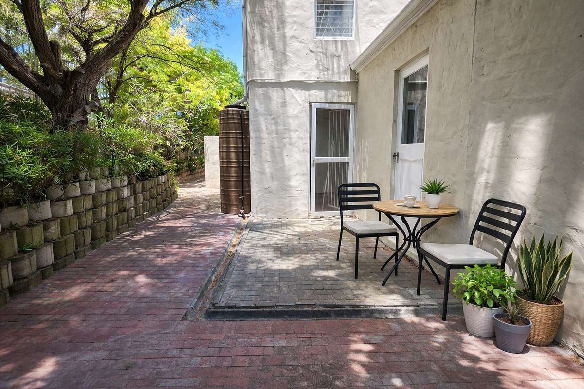A private rear patio area featuring brick paving, a water tank, and direct access to the apartment through a glass-panelled door.