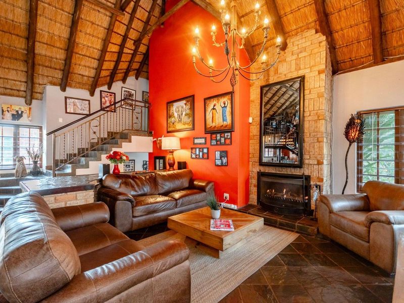 Spacious living room featuring a high thatched ceiling with exposed rafters, a prominent brick fireplace, and elegant slate tile flooring.