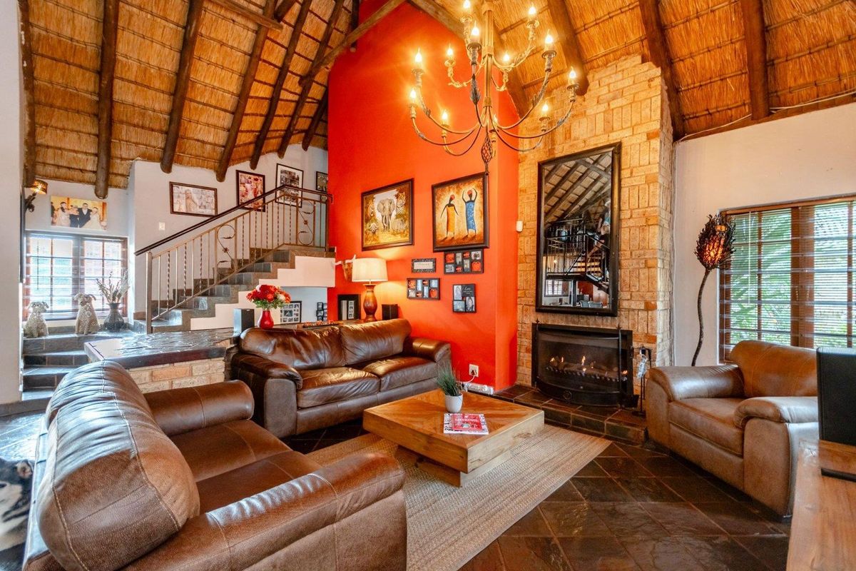 Spacious living room featuring a high thatched ceiling with exposed rafters, a prominent brick fireplace, and elegant slate tile flooring.