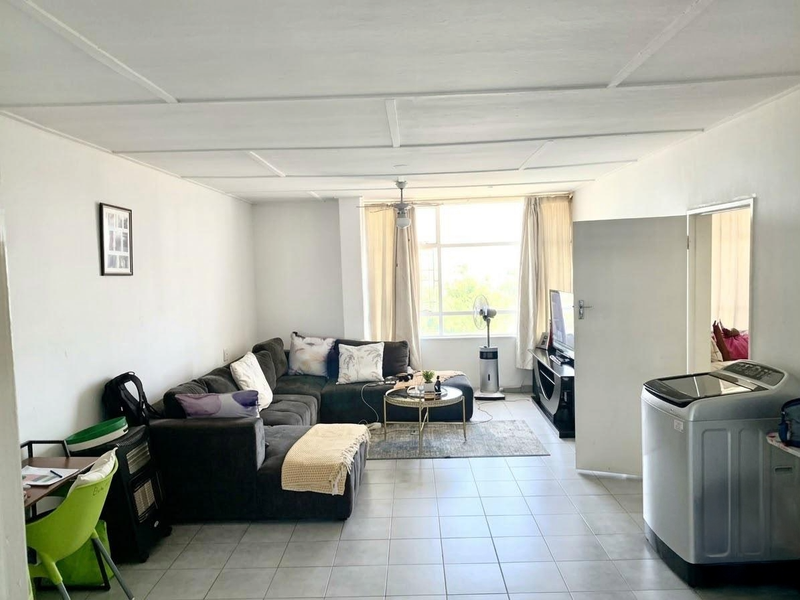 A spacious living area featuring tiled flooring, a ceiling fan, and large windows that provide ample natural light.