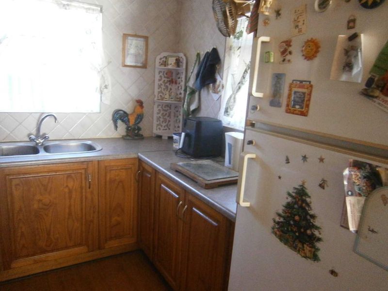 A dated kitchen featuring timber cabinetry, laminate countertops, and a double bowl sink with tiled splashback.