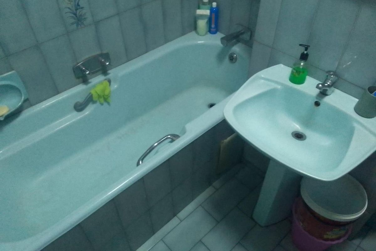 A dated bathroom featuring a light blue bathtub and matching pedestal basin with tiled walls and flooring.
