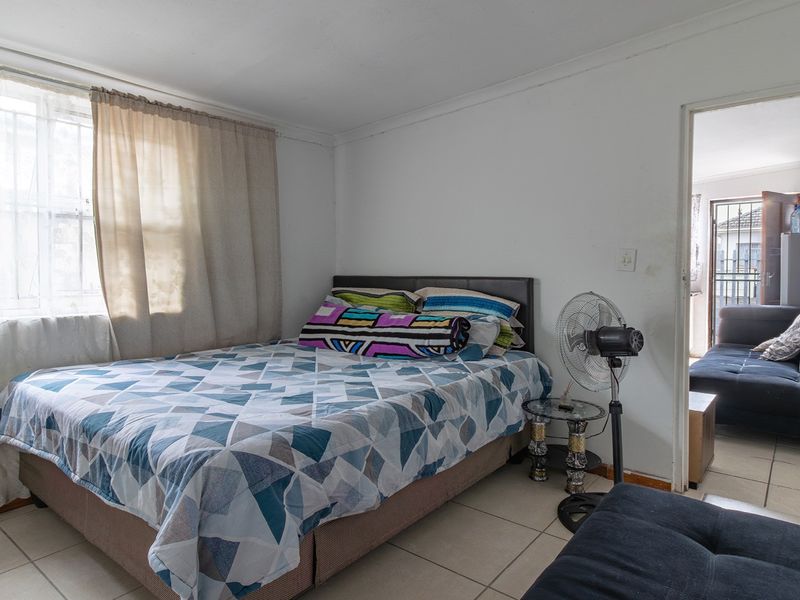 A bedroom featuring tiled flooring and a window, with an adjacent room visible through the doorway.
