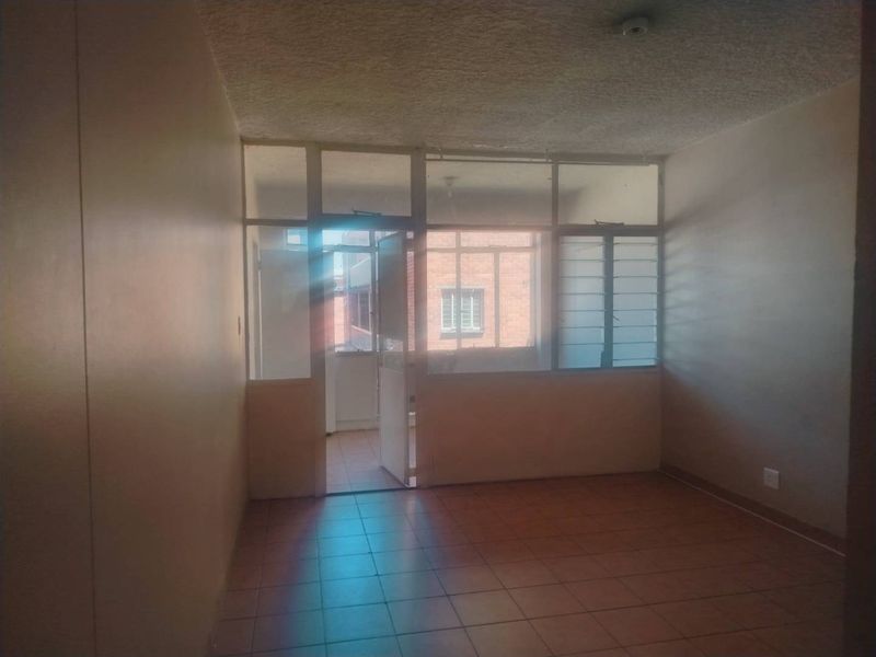 An empty living room featuring tiled flooring and a glass partition wall leading to an enclosed balcony area, requiring cosmetic updates.