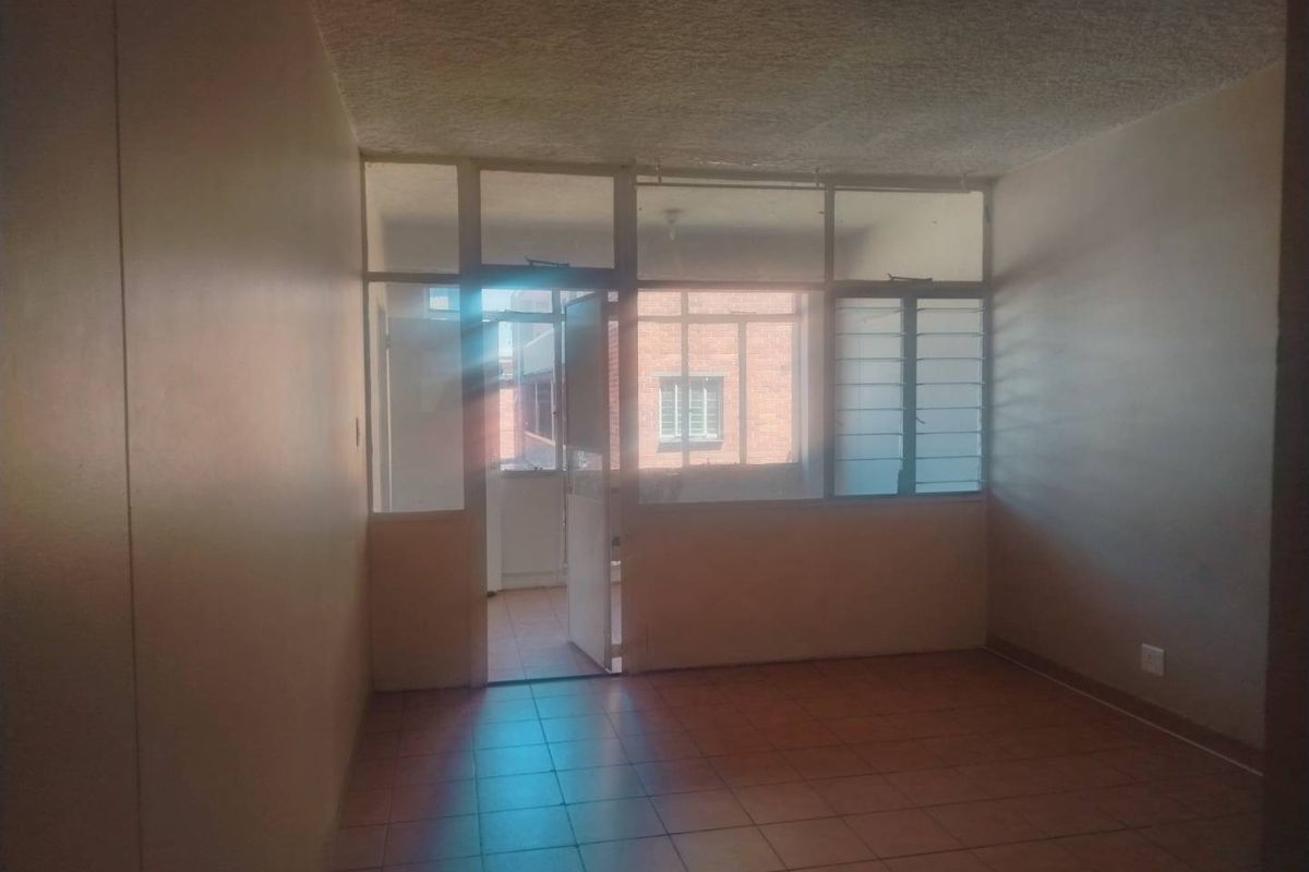 An empty living room featuring tiled flooring and a glass partition wall leading to an enclosed balcony area, requiring cosmetic updates.