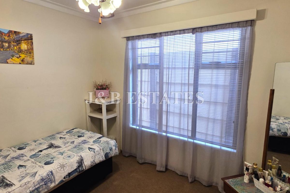 A standard bedroom featuring neutral walls, carpeted flooring, and a large window with fitted blinds and curtains.