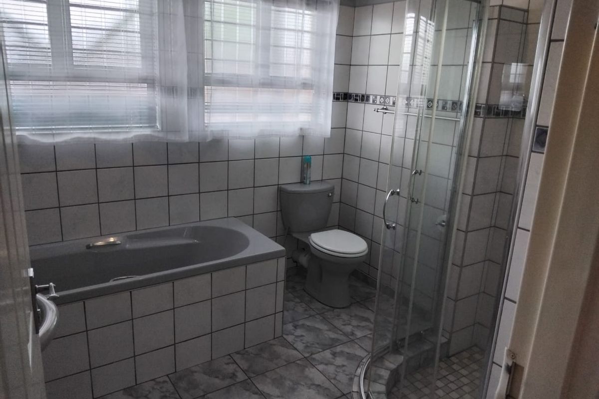 A functional bathroom featuring a built-in bathtub, a separate glass-enclosed shower, and a toilet, finished with tiled walls and flooring.