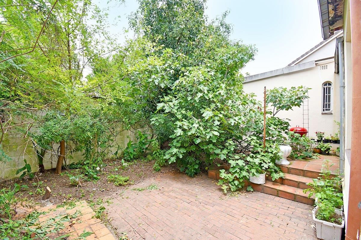 A private rear garden area featuring a brick-paved patio, tiered steps, and established greenery adjacent to the main house structure.