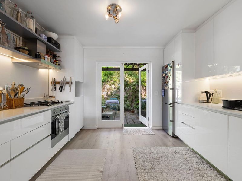 Modern galley-style kitchen featuring sleek white cabinetry, stone countertops, integrated appliances, and direct access to a private rear courtyard.