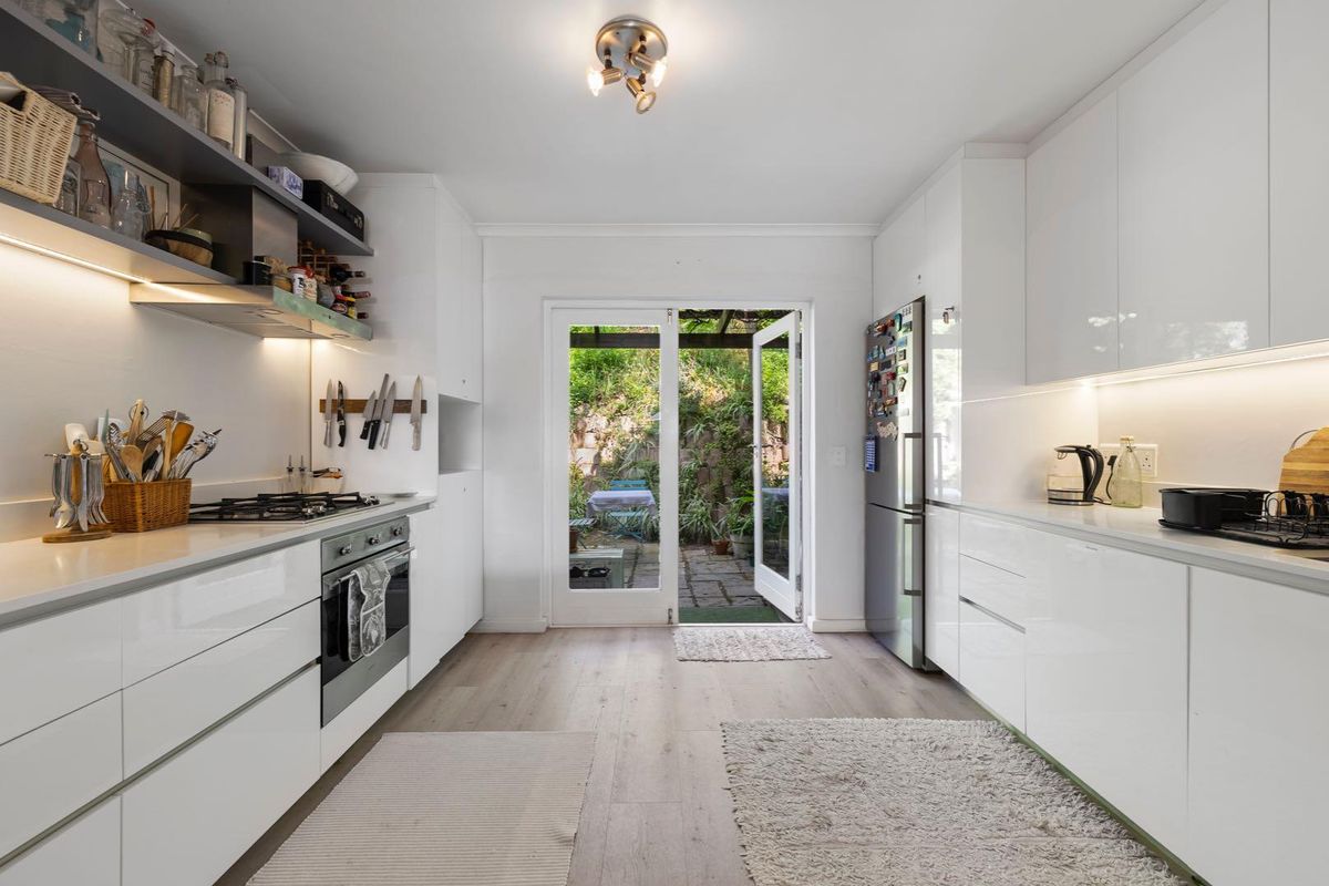 Modern galley-style kitchen featuring sleek white cabinetry, stone countertops, integrated appliances, and direct access to a private rear courtyard.
