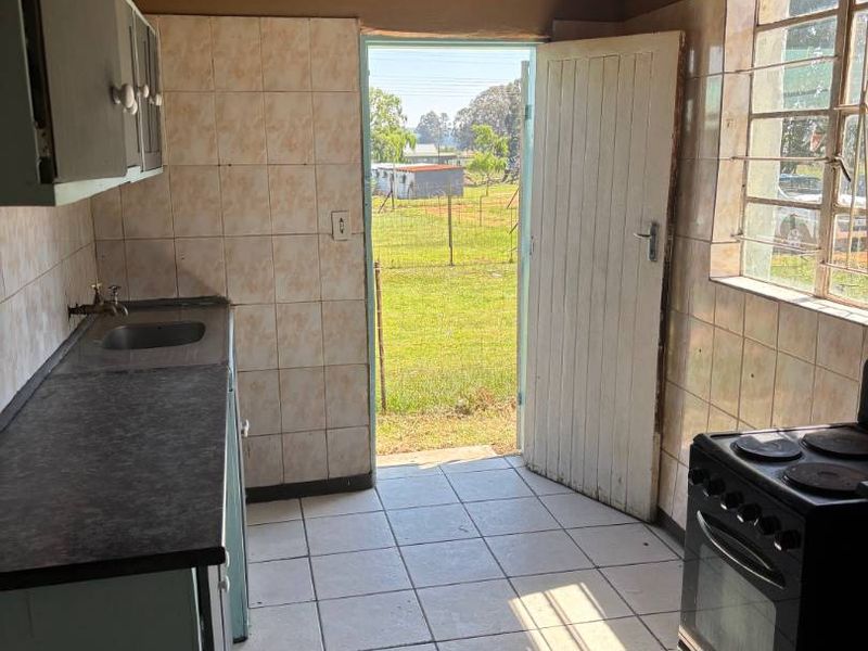A dated kitchen featuring tiled flooring, timber ceiling, and basic cabinetry, with direct access to the rear garden area.