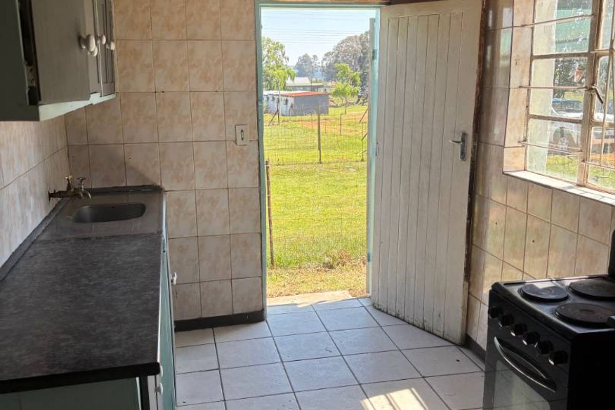 A dated kitchen featuring tiled flooring, timber ceiling, and basic cabinetry, with direct access to the rear garden area.