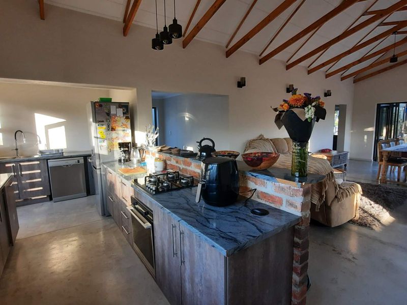 Spacious open-plan living area featuring exposed timber rafters, polished concrete floors, and a modern kitchen with stone countertops and a brick breakfast bar.