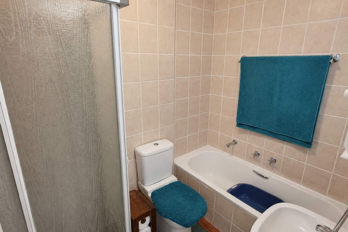 A functional bathroom featuring a built-in bathtub, shower enclosure, and standard toilet with neutral wall tiling.