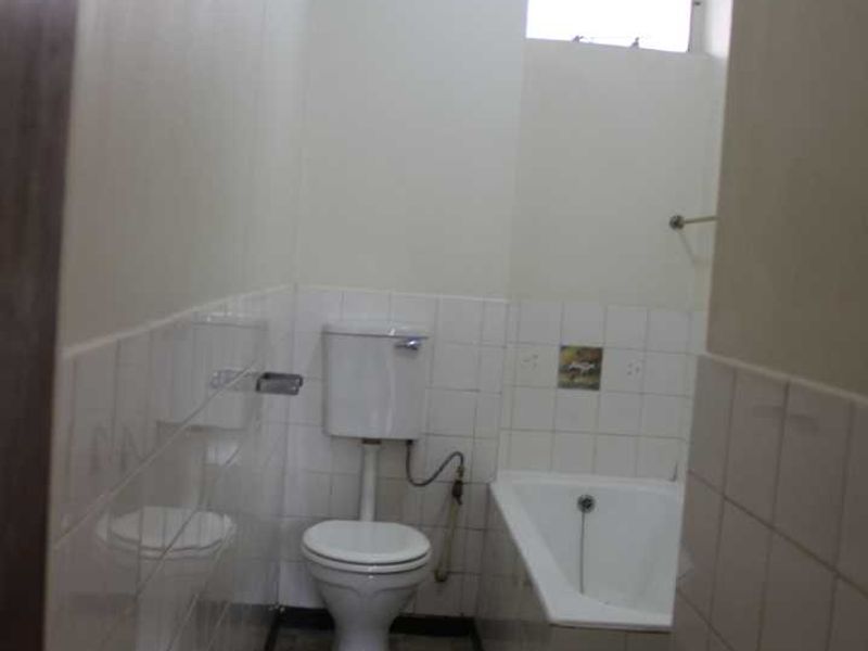 A compact, dated bathroom featuring a standard bathtub, toilet, and tiled finishes, offering potential for a modern renovation.