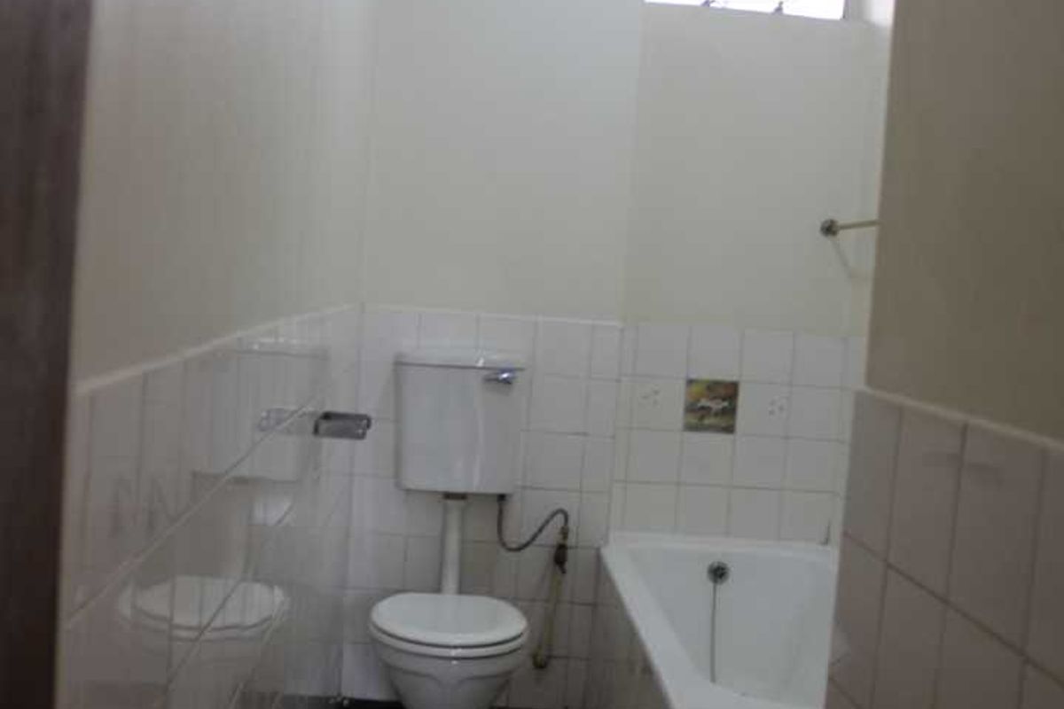 A compact, dated bathroom featuring a standard bathtub, toilet, and tiled finishes, offering potential for a modern renovation.