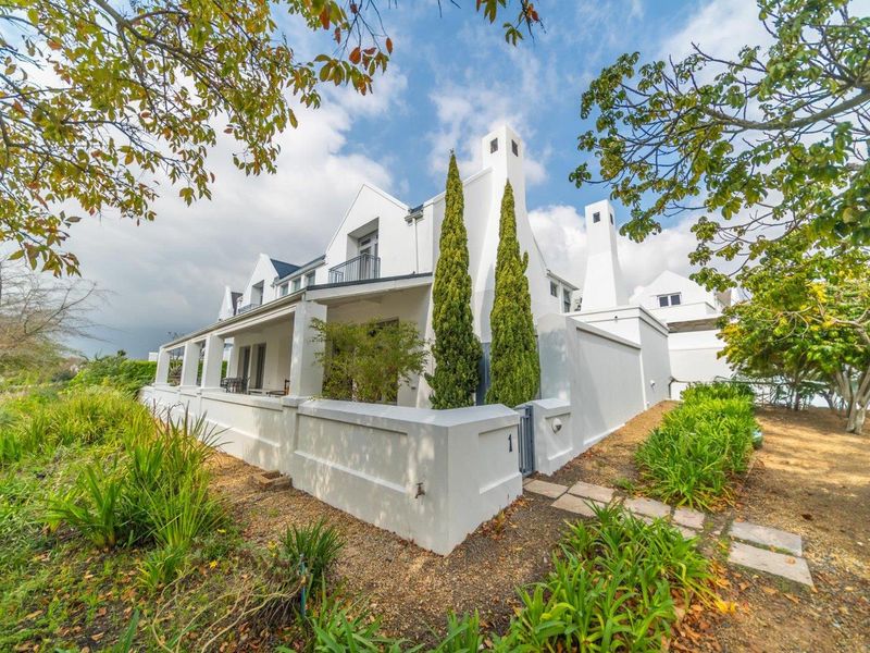A well-maintained white exterior facade featuring a covered patio, balcony, and prominent chimneys, set within a landscaped garden environment.