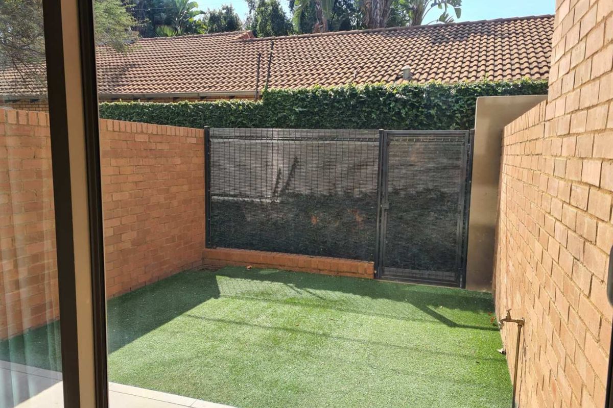 A private, low-maintenance courtyard featuring artificial turf, brick boundary walls, and a secure gate, accessible directly from the interior living space.