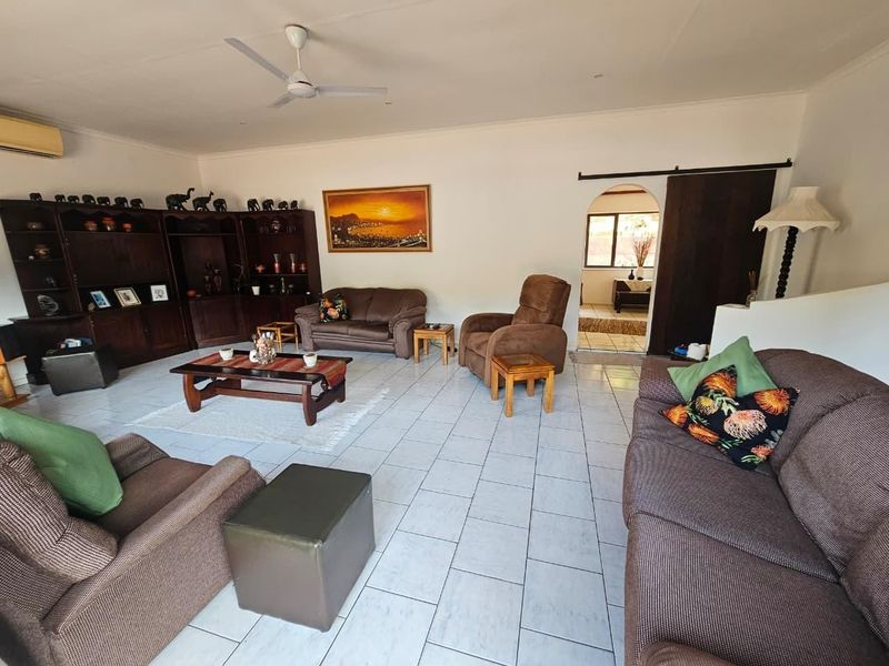 Spacious living room featuring tiled flooring, a ceiling fan, built-in wooden cabinetry, and an arched doorway leading to an adjacent area.