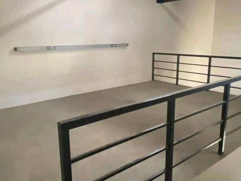 An open-plan mezzanine utility space featuring exposed steel roof trusses, concrete flooring, and a secure metal balustrade with natural light from a skylight.