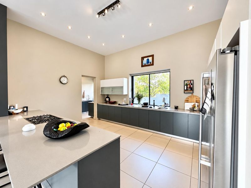 Modern kitchen featuring a large island, stone countertops, dark cabinetry, gas cooktop, and recessed lighting, with an adjacent scullery area.
