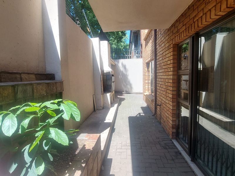 A paved outdoor patio area featuring a built-in braai, exposed brick wall, and sliding glass door access to the interior.