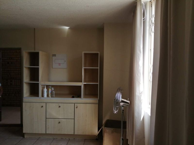 Living area featuring built-in cabinetry, tiled flooring, and a window with a security gate, offering a functional space with potential for modernization.
