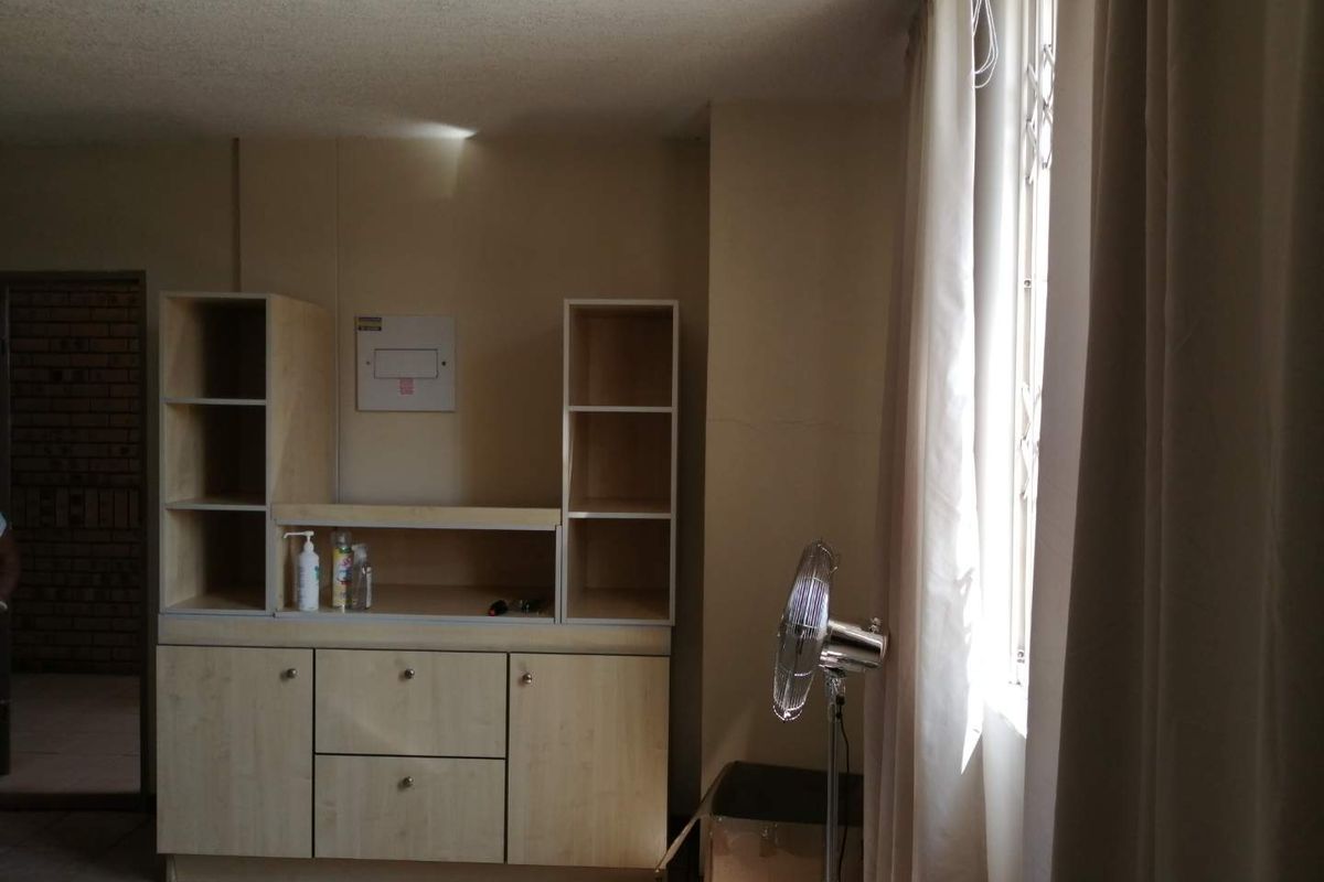 Living area featuring built-in cabinetry, tiled flooring, and a window with a security gate, offering a functional space with potential for modernization.