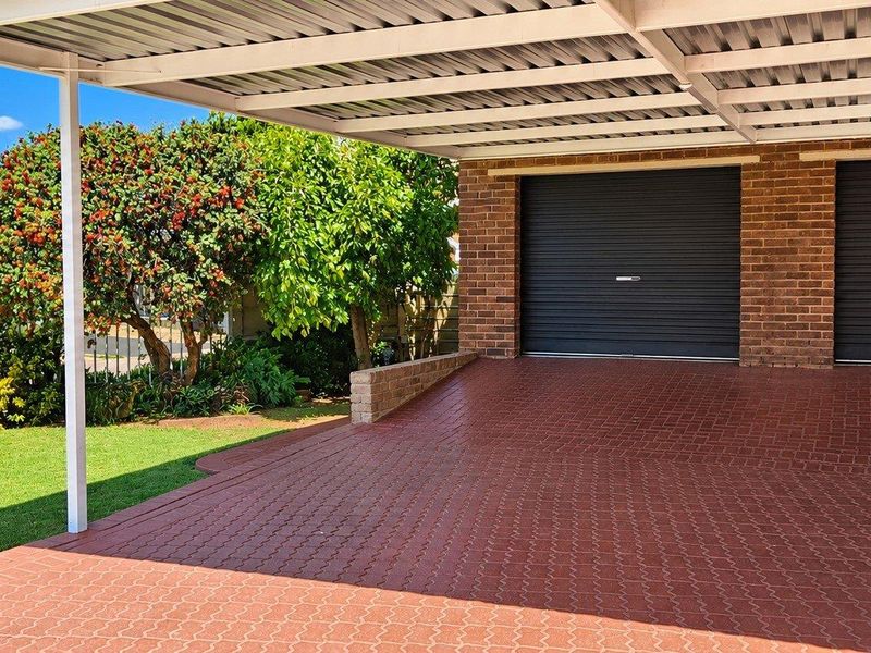 A well-maintained double garage featuring a paved driveway, metal carport cover, and brick exterior, set within a neat residential garden area.