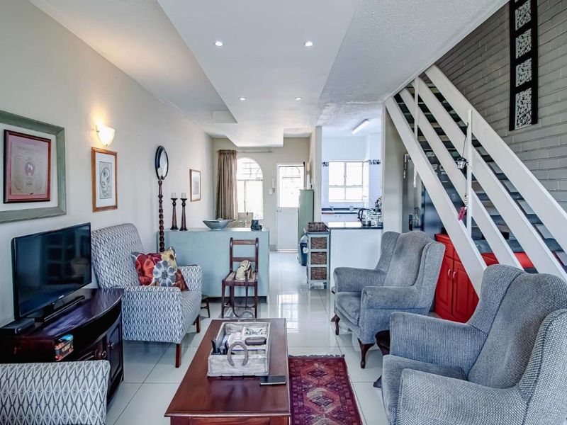 Open-plan living area featuring tiled floors, recessed lighting, and a staircase with a feature brick wall, leading through to the kitchen area.