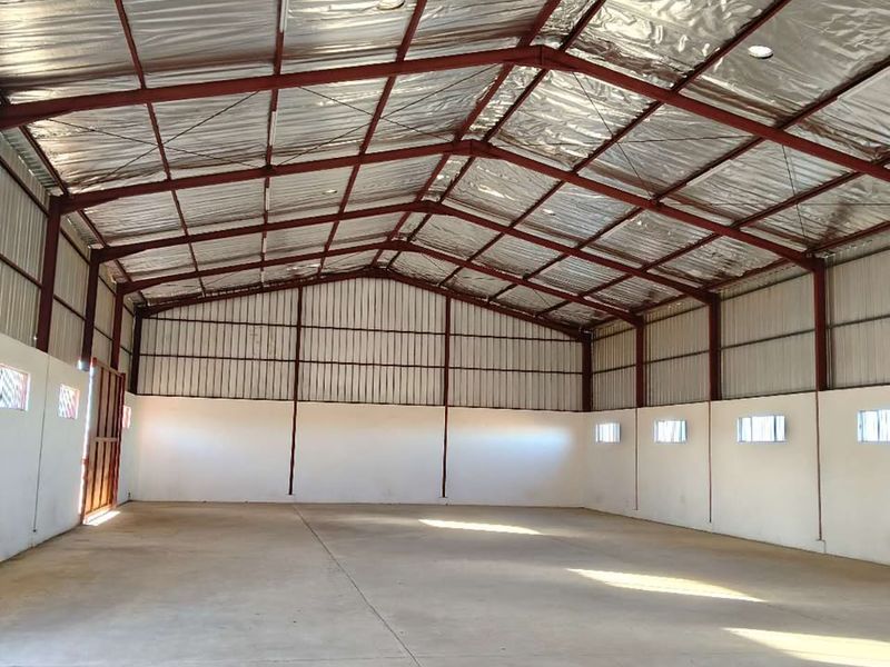 A spacious, empty utility shed or workshop featuring a steel portal frame, concrete flooring, and insulated metal roofing with high-level windows.
