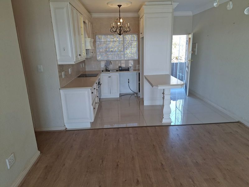 Open-plan kitchen featuring white cabinetry, stone countertops, and a breakfast bar, seamlessly transitioning from tiled kitchen area to laminate living space.