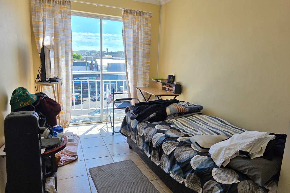 A functional bedroom featuring tiled flooring and a sliding glass door that opens onto a small balcony with street views.