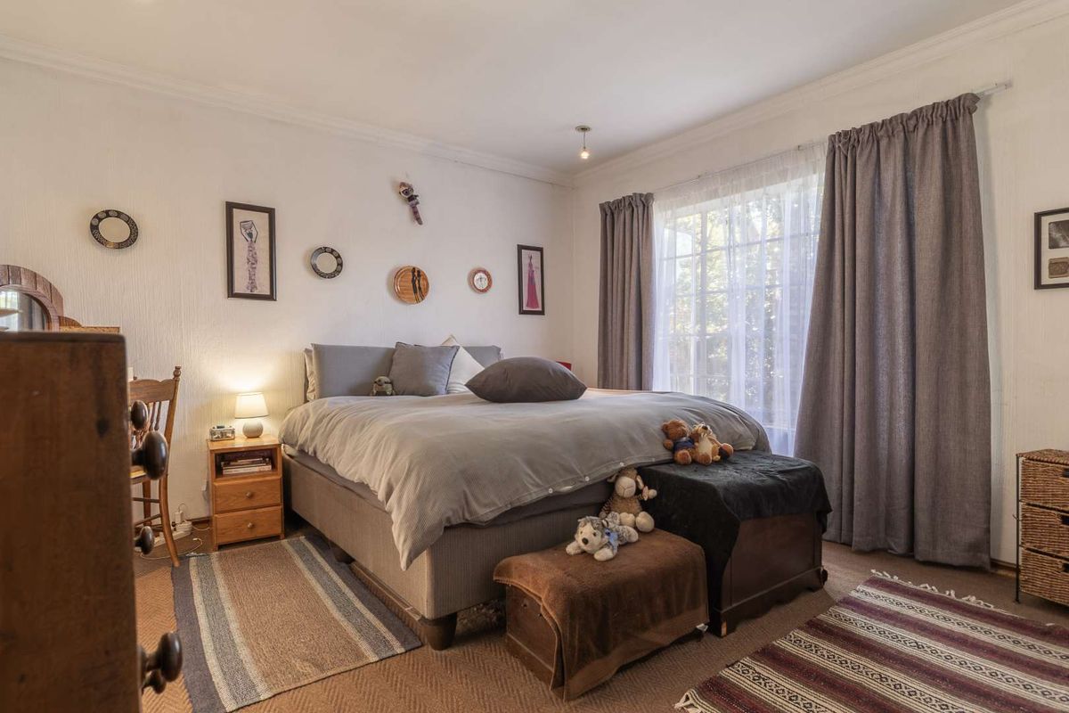 A well-lit bedroom featuring neutral wall finishes, crown molding, and large windows with curtains, providing a comfortable and functional living space.