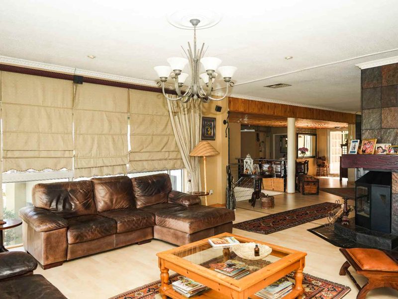 Spacious living room featuring a stone-clad fireplace, decorative ceiling rose with chandelier, and timber ceiling accents, creating a warm and traditional atmosphere.