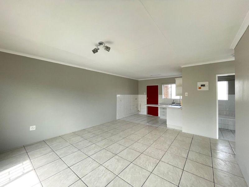An open-plan living and kitchen area featuring neutral tiled flooring, built-in kitchen cabinetry, and a functional layout ready for personalization.