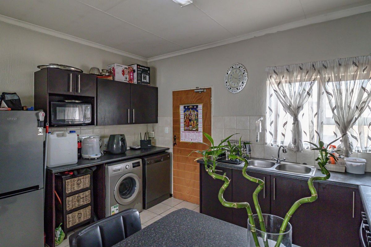 Functional kitchen featuring dark cabinetry, integrated sink, tiled backsplash, and space for laundry appliances, offering a practical layout for daily use.