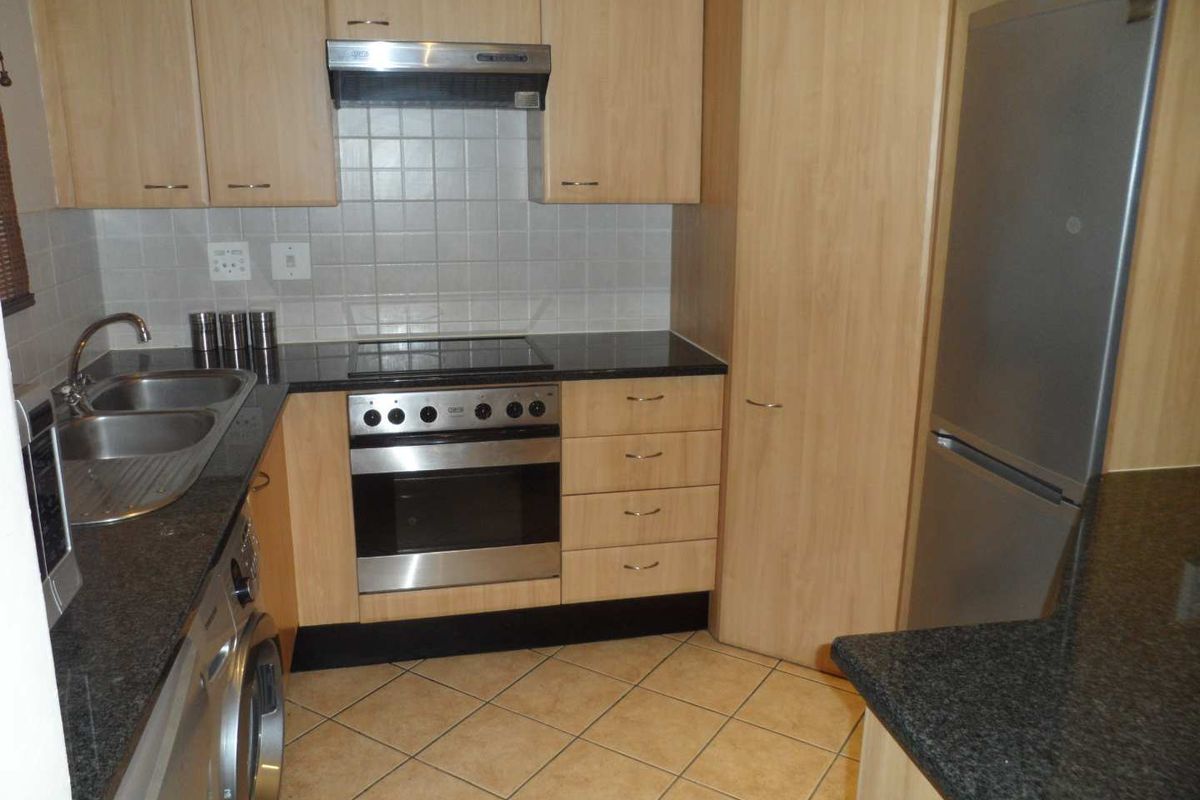 Compact kitchen featuring light wood laminate cabinetry, granite countertops, tiled backsplash, and integrated stainless steel appliances including an oven and hob.