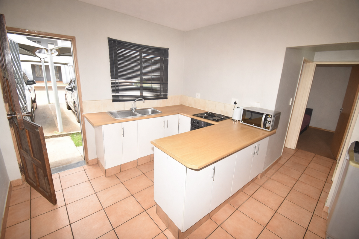 Functional kitchen featuring laminate countertops, a double basin sink, built-in hob, and tiled flooring with direct access to the exterior.