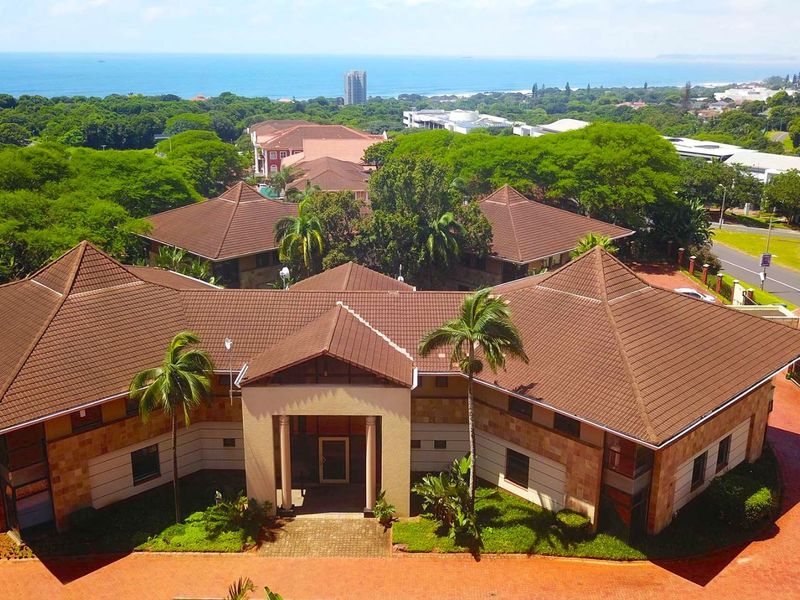 Aerial view of a professional office complex featuring a tiled roof, stone facade, and paved driveway, set within a landscaped environment.